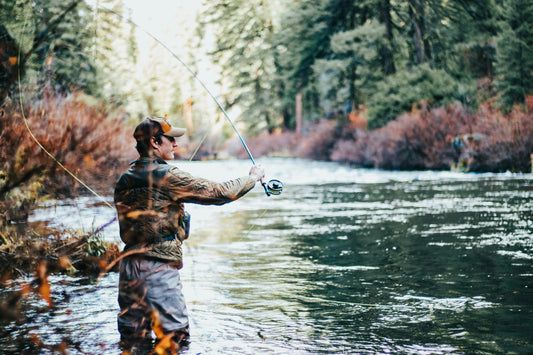 fisherman casting a rod into a river in waders