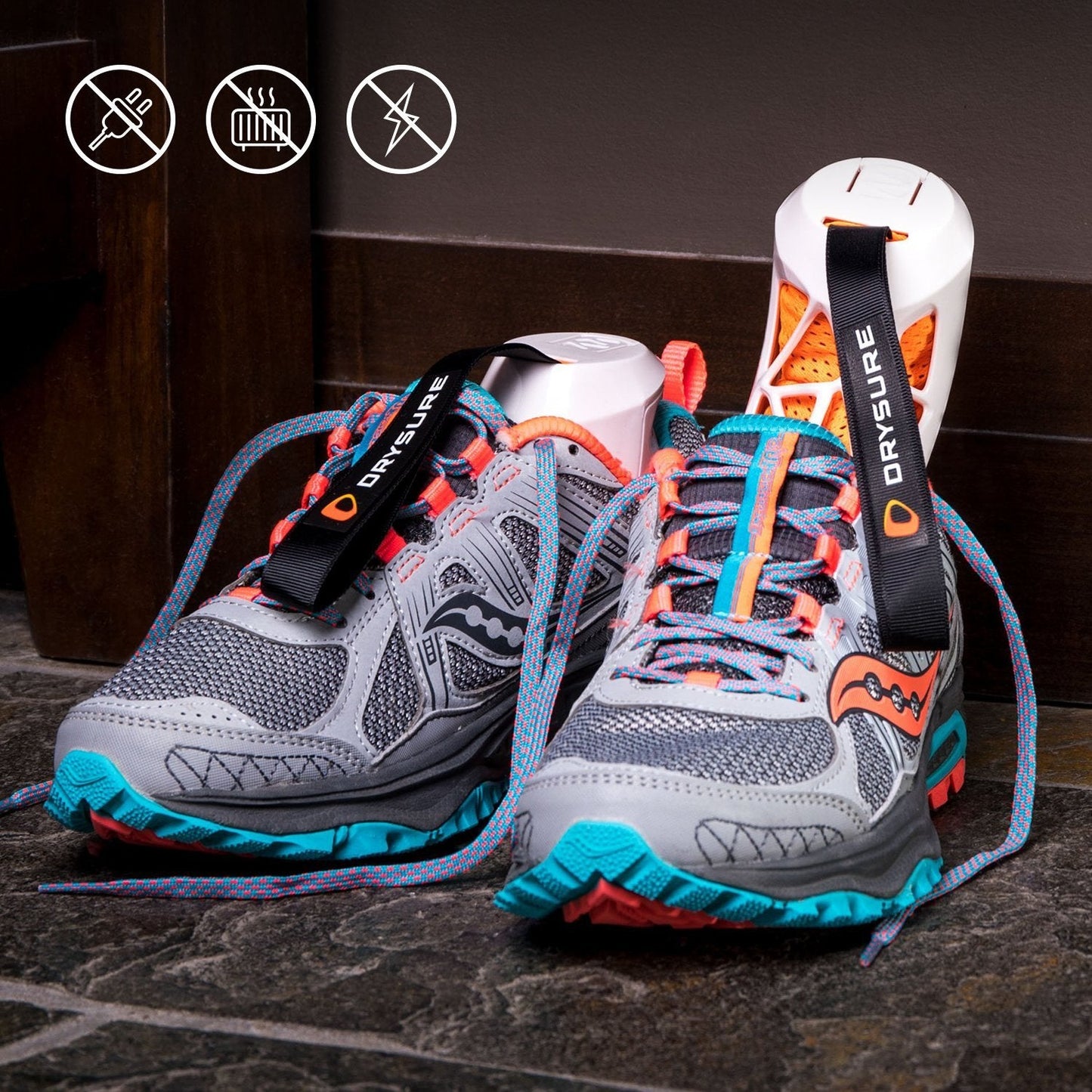 Gray hiking or running shoes with colorful accents on a dark surface. White and orange drysure active shoe dryers are in the shoes featuring DRYSURE branding.