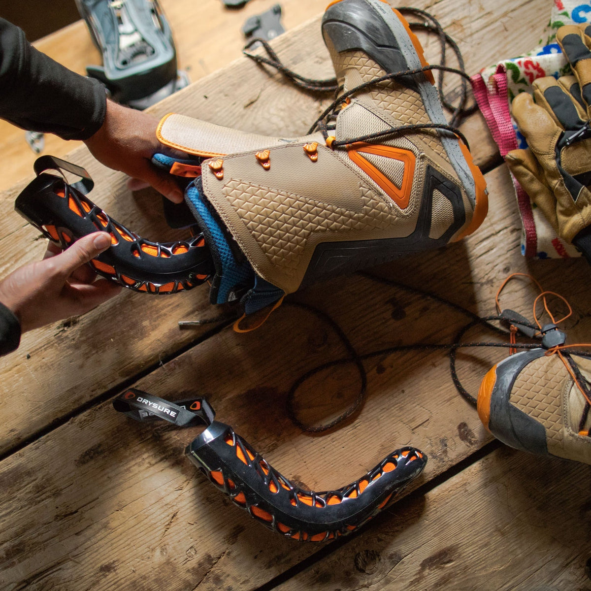 Person inserting Drysure Extreme in black and orange into a pair of brown snowboard boots on a wooden table