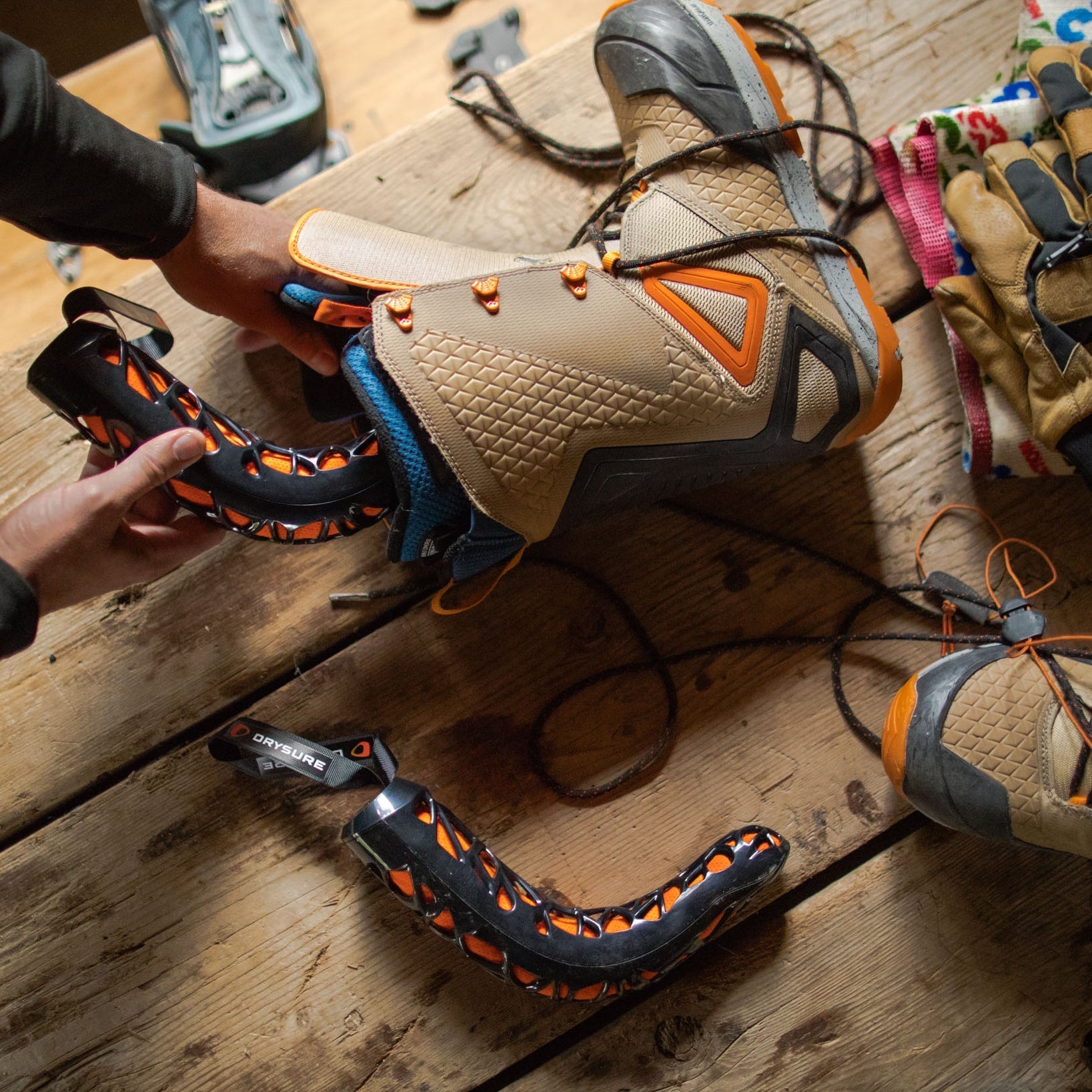 Person inserting Drysure Extreme in black and orange into a pair of brown snowboard boots on a wooden table