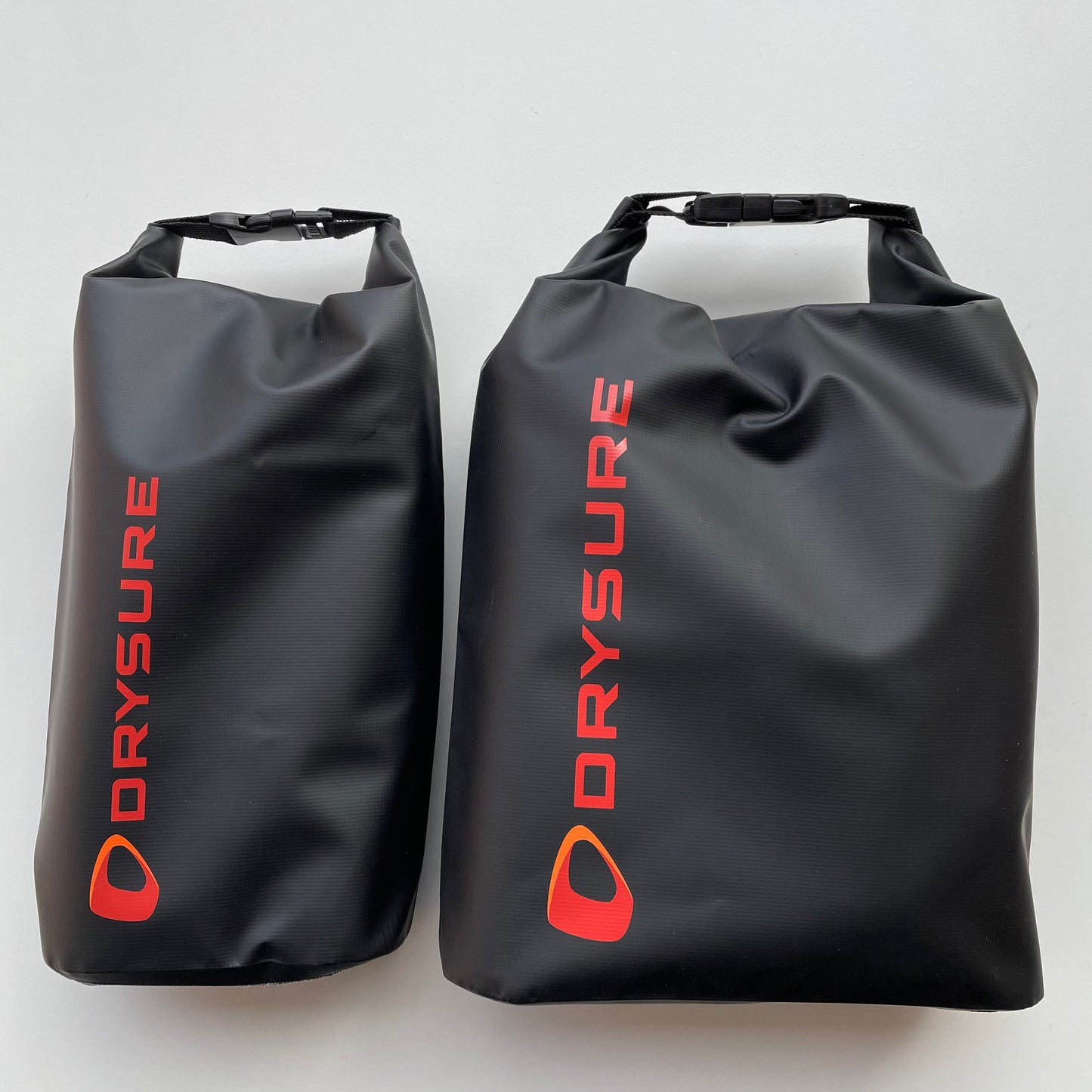 Two black DrySure dry bags with red and white brand logo, one large and one small, designed for storing laundry and personal items.